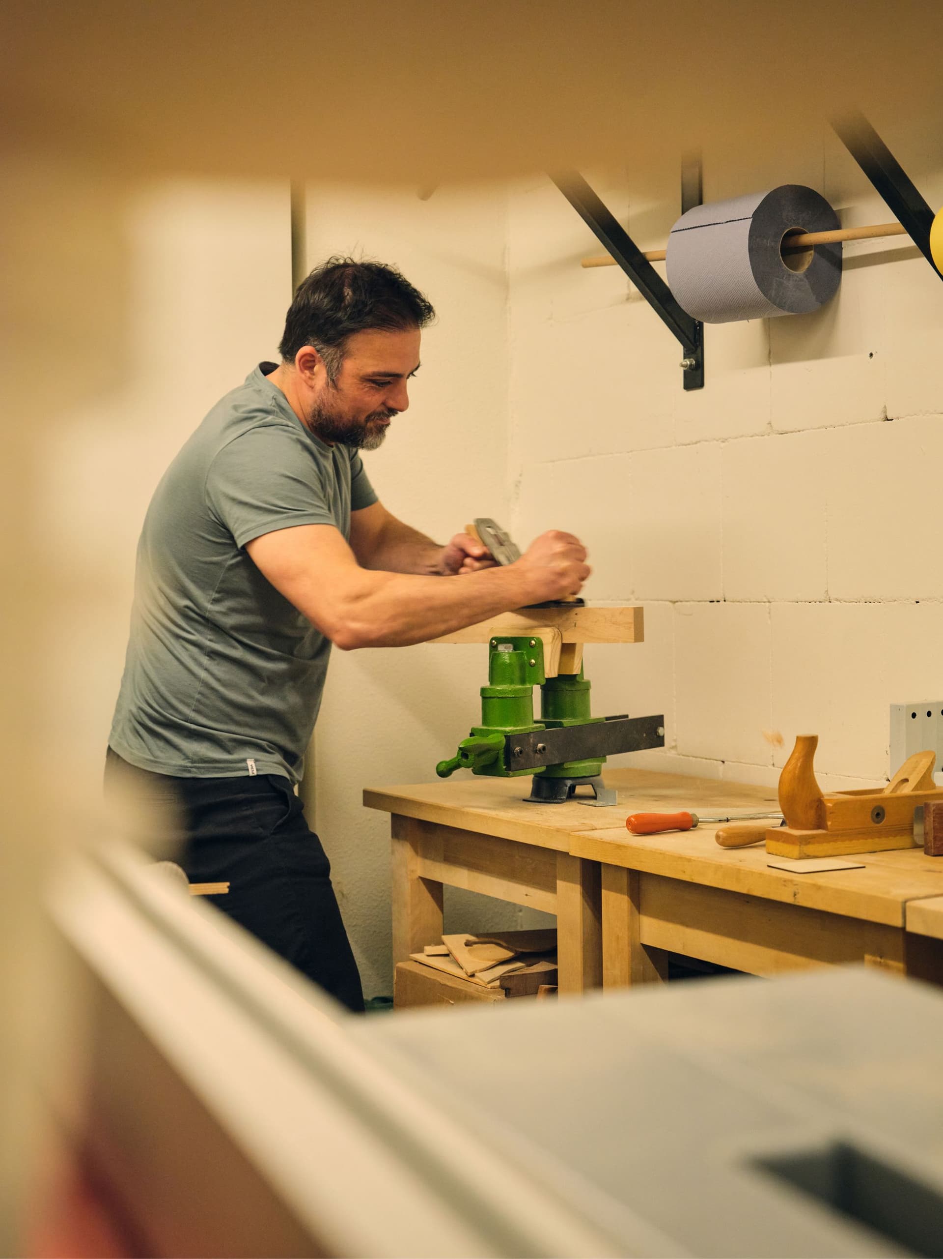 Person working with a vise and hand tools at a wooden workbench in a workshop