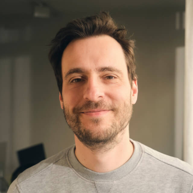 Person with short brown hair and a beard, wearing a grey sweatshirt indoors