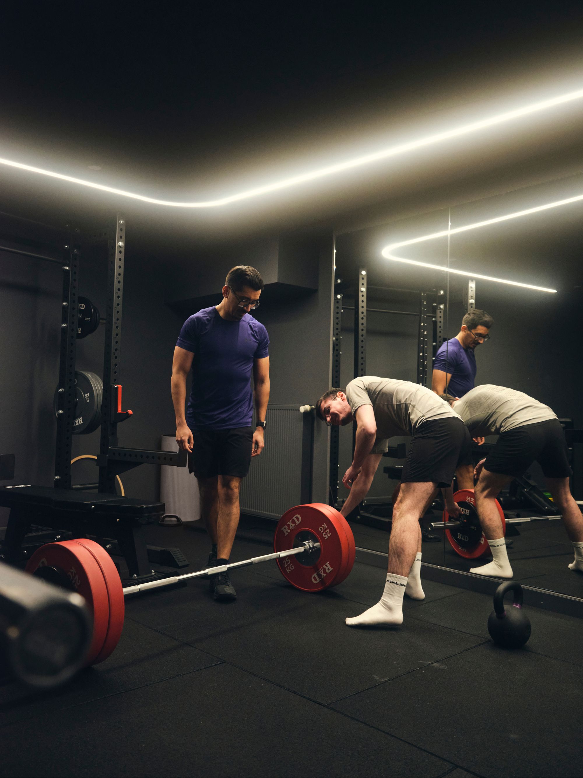 Two people in a gym setting, one preparing to lift a barbell while the other observes