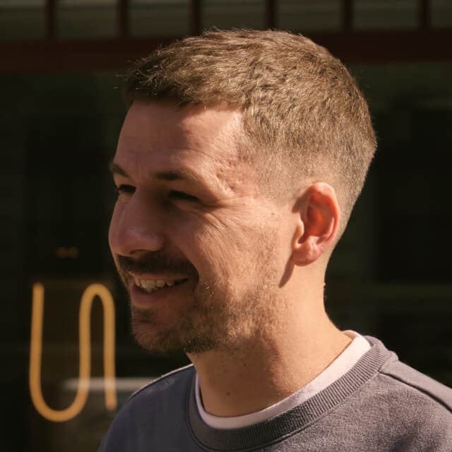 Person with short light brown hair, wearing a grey sweatshirt, standing outdoors